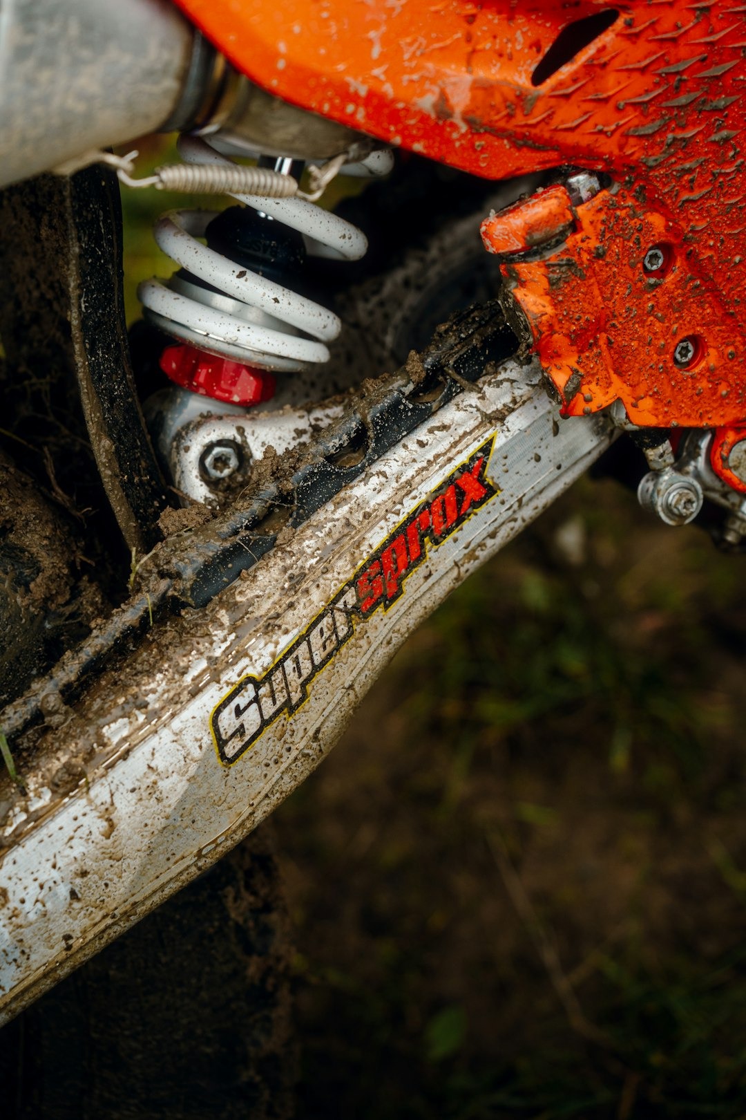 Mud covered dirt bike suspension with a white coil spring.